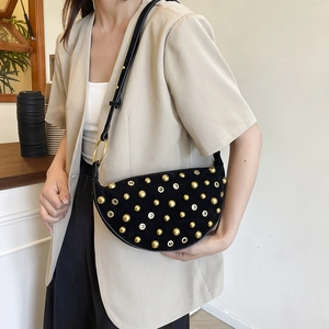 Fashionable black suede half-moon shoulder bag with golden studs on a female model
