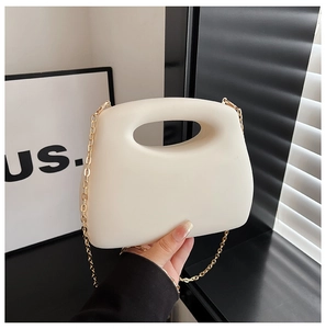 Detail view of a cream acrylic clutch with gold chain strap and hollow handle design