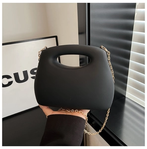 Detail of matte black acrylic box bag with hollow round handle and gold chain