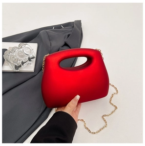 Detail of red acrylic clutch bag with oval cutout handle and thin gold chain strap