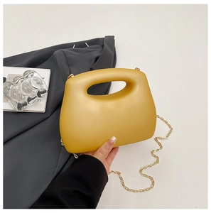Detail of yellow acrylic box bag featuring hollow handle and gold chain on gray suit