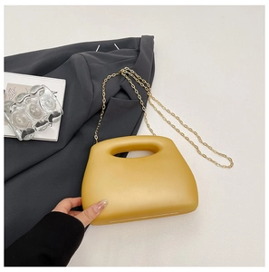 Detail of yellow acrylic evening bag with hollow handle and gold chain on grey fabric