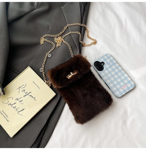 Close-up of brown plush phone bag with golden metal buckle and chain strap on fabric
