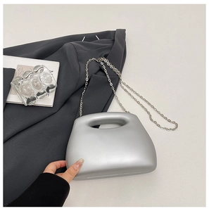 Macro view of matte silver trapezoid hard-shell bag with integrated handle and chain