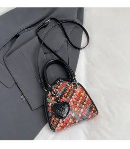 Détail du sac coquille en cuir tressé coloré avec poignées noires et breloque cœur