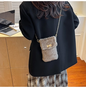 Brown faux fur crossbody bag shown with gold chain strap on a desk lifestyle setting
