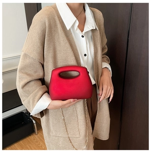 Detail of red acrylic clutch bag with hollow handle and gold chain on neutral outfit