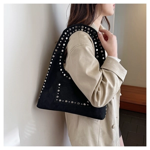 Close-up of black suede hobo bag with silver studs worn by a model in a beige trench coat