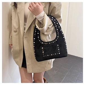 Detail of black suede crescent bag with silver rivet studs on a beige coat model