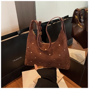 Detailed close-up of brown suede shoulder bag with gold rivets and bow detail