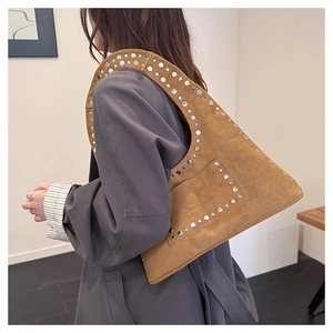 Detail of silver rivets on a brown suede tote bag worn by a model in a grey coat