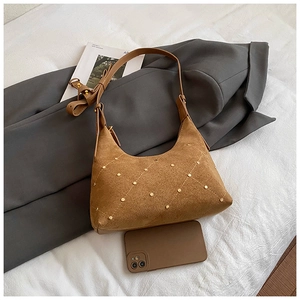 Detail of brown suede crescent bag with gold studs and adjustable strap next to a phone