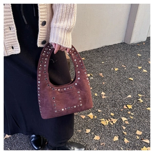 Close-up of brown suede shoulder bag with silver rivet studs and autumn leaf background
