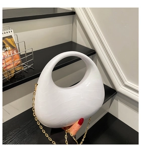 Detail of white marble acrylic crescent bag with golden chain strap on a modern backdrop
