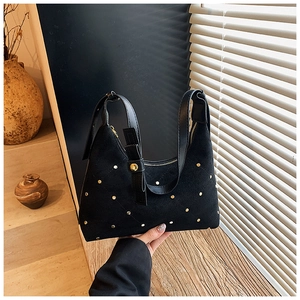 Detail of black suede underarm bag with gold studs and zipper against a sunny backdrop