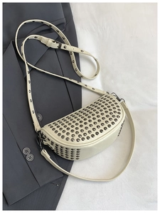Detail shot of punk style beige crescent bag with metallic studs on leather surface