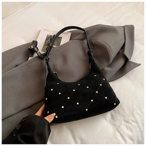 Detail of matte black quilted bag with gold rivets on grey suit blazer background
