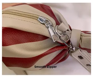 Gros plan détaillé sur le zip argenté et le cuir rayé rouge de la sacoche bandoulière