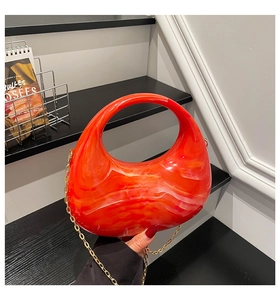 Detail view of orange marble acrylic handbag with integrated circular handle and gold chain