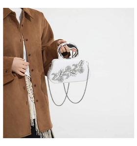 Close-up of a white evening bag with rhinestone flowers held by a model in a suede jacket