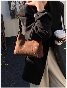 Detail of dark brown suede shoulder bag with gold rivets and adjustable leather strap