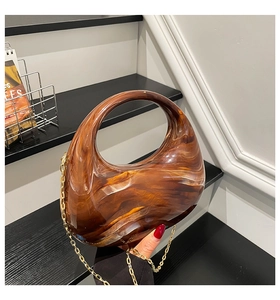 Detail of amber acrylic crescent bag with marble texture and gold chain link strap