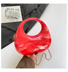 Detail of red marble acrylic half-moon bag with gold chain strap on grey blazer
