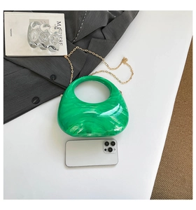 Detailed view of green marble acrylic clutch with gold chain next to a mobile phone