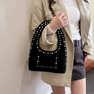 Women's black rivet hobo bag with matte finish shown on shoulder with beige coat