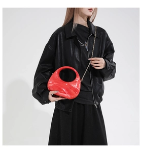 Detail of red marble acrylic half-moon bag with gold chain strap on female model