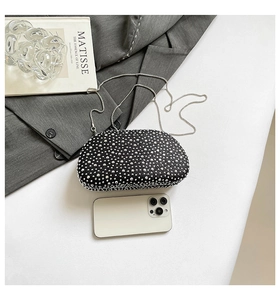 Detail of black rhinestone evening clutch with silver chain next to smartphone for scale