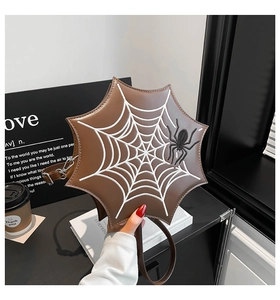 Detail of a brown octagon spiderweb crossbody bag with white stitching and spider ornament