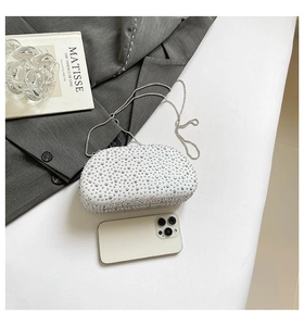 Flat lay of white rhinestone clutch bag with silver chain next to a mobile phone