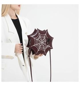 Deep burgundy spider web crossbody bag with white print and decorative spider worn by model