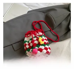 Detail of crochet bucket bag featuring red, white, and green plaid weave and floral pendant