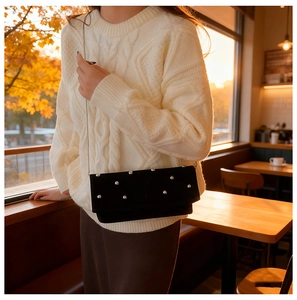 Detail of black suede shoulder bag with silver studs and chain strap in sunset light