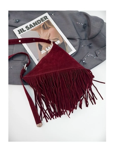 Detail of burgundy suede shoulder bag featuring long fringe accents and metal strap ring