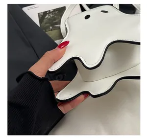 Detailed close-up of precise black stitching on a white leather ghost-shaped shoulder bag