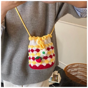 Detail of crochet bucket bag featuring red and white shell stitch with strawberry charm