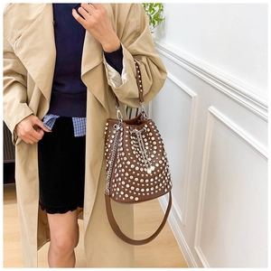 Brown rivet bucket bag with silver rhinestones and pearl drawstring worn on trench coat