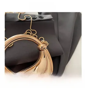 Detail of a golden crescent evening bag featuring a round metal handle and snake chain