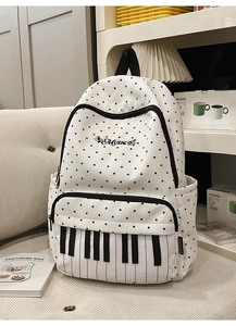 Detail of white canvas backpack featuring black polka dots and piano keyboard pocket design