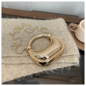 Golden crescent evening bag with mirror finish and elegant round handle on beige knitwear