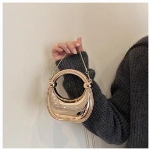 Detail of a half-moon golden clutch bag with horseshoe handle and fine metal chain strap
