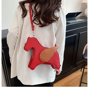 Detail of red winged horse-shaped crossbody bag shown on a white blazer outfit