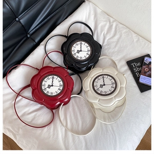 Three flower-shaped crossbody clock bags in red, black, and white colors on a white fabric
