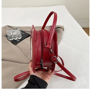 Detail view of red clock-shaped PU leather handbag with zipper and metal hardware hooks