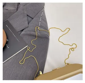 Detail of a chic gold acrylic clutch bag with a slim metal chain on a grey blazer