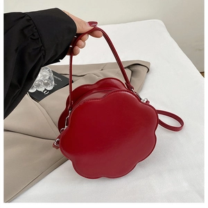 Detail of red flower-shaped leather handbag with sleek metallic strap clips and handle