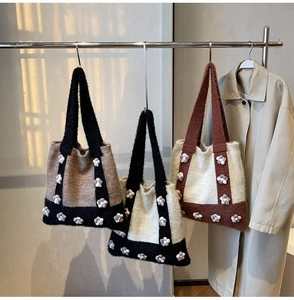 Detail of knitted tote bags with 3D floral accents in black, brown, and cream colors